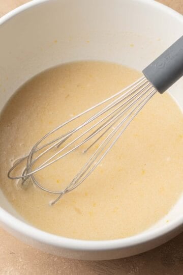 wet ingredients in a white bowl whisked together by metal whisk.