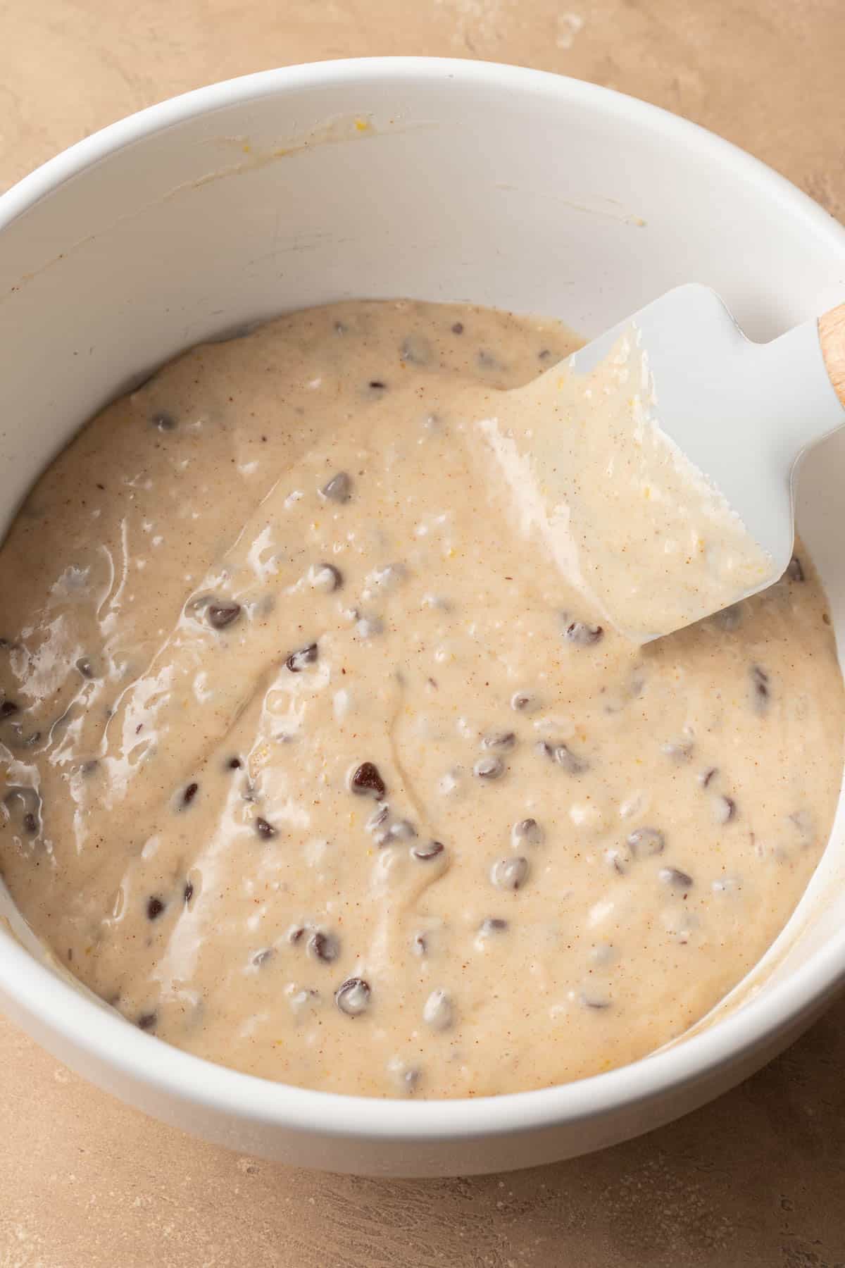 muffin batter fully mixed with mini chocolate chips added, in a white bowl.