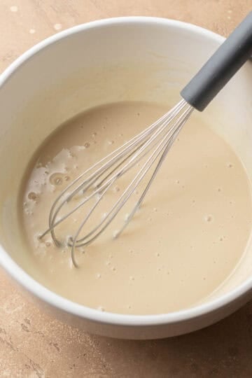 sweetened condensed milk mixture in a white bowl with a metal whisk.
