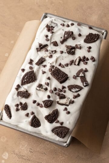 oreo ice cream in a loaf pan with oreos and chocolate chips sprinkled on top before going in the freezer