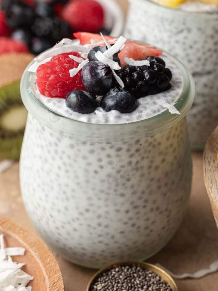 Chia seed breakfast bowl in a glass jar that is topped with mixed berries and coconut flakes.