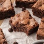 A close up of the fudge brownie that has a bite taken out of it sitting on parchment paper.
