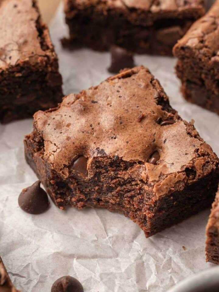 A close up of the fudge brownie that has a bite taken out of it sitting on parchment paper.