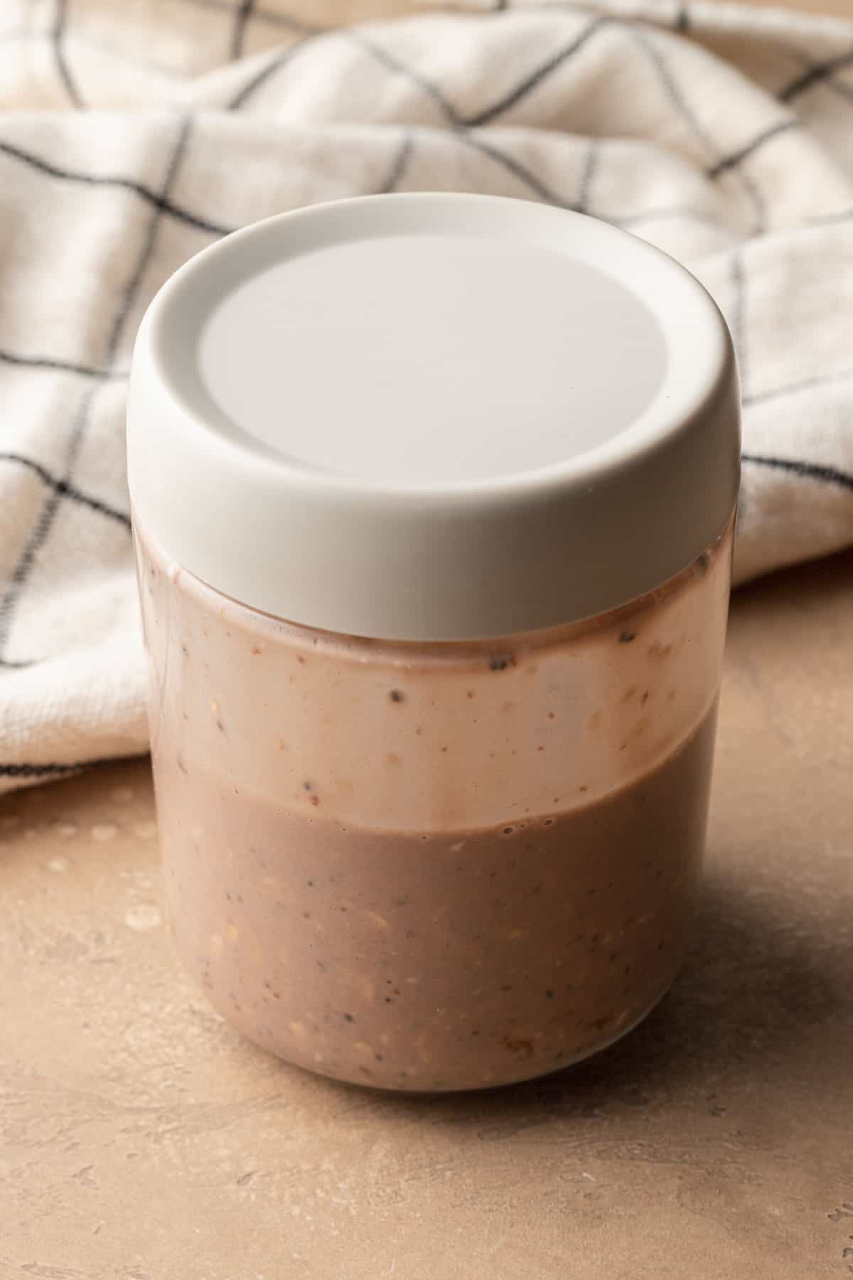 Dry and wet ingredients for chocolate protein overnight oats in mason jar with lid on top.