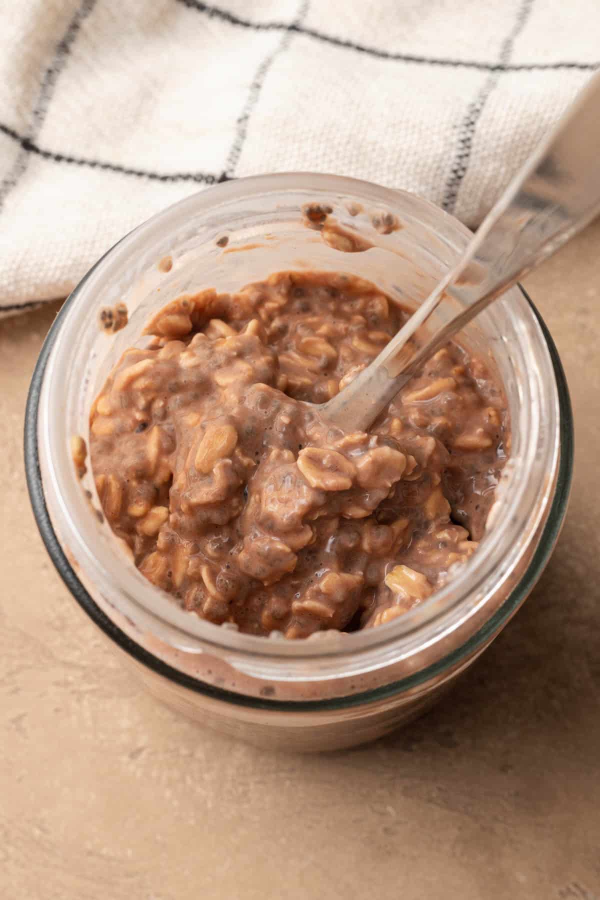 Chocolate protein overnight oats that are ready to be eaten in a mason jar with a spoon.