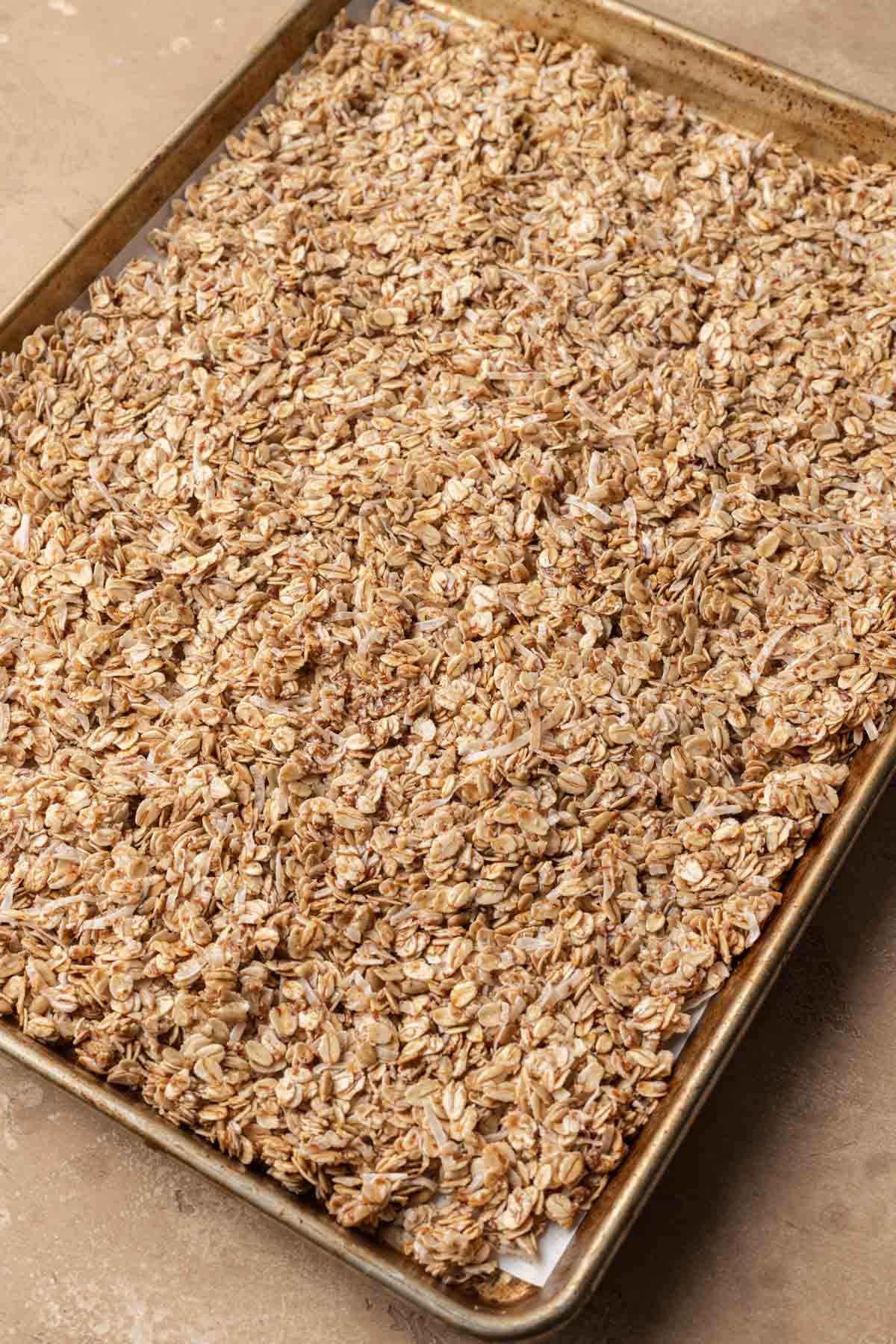 Homemade granola spread out evenly on a baking sheet ready to be put in the oven.