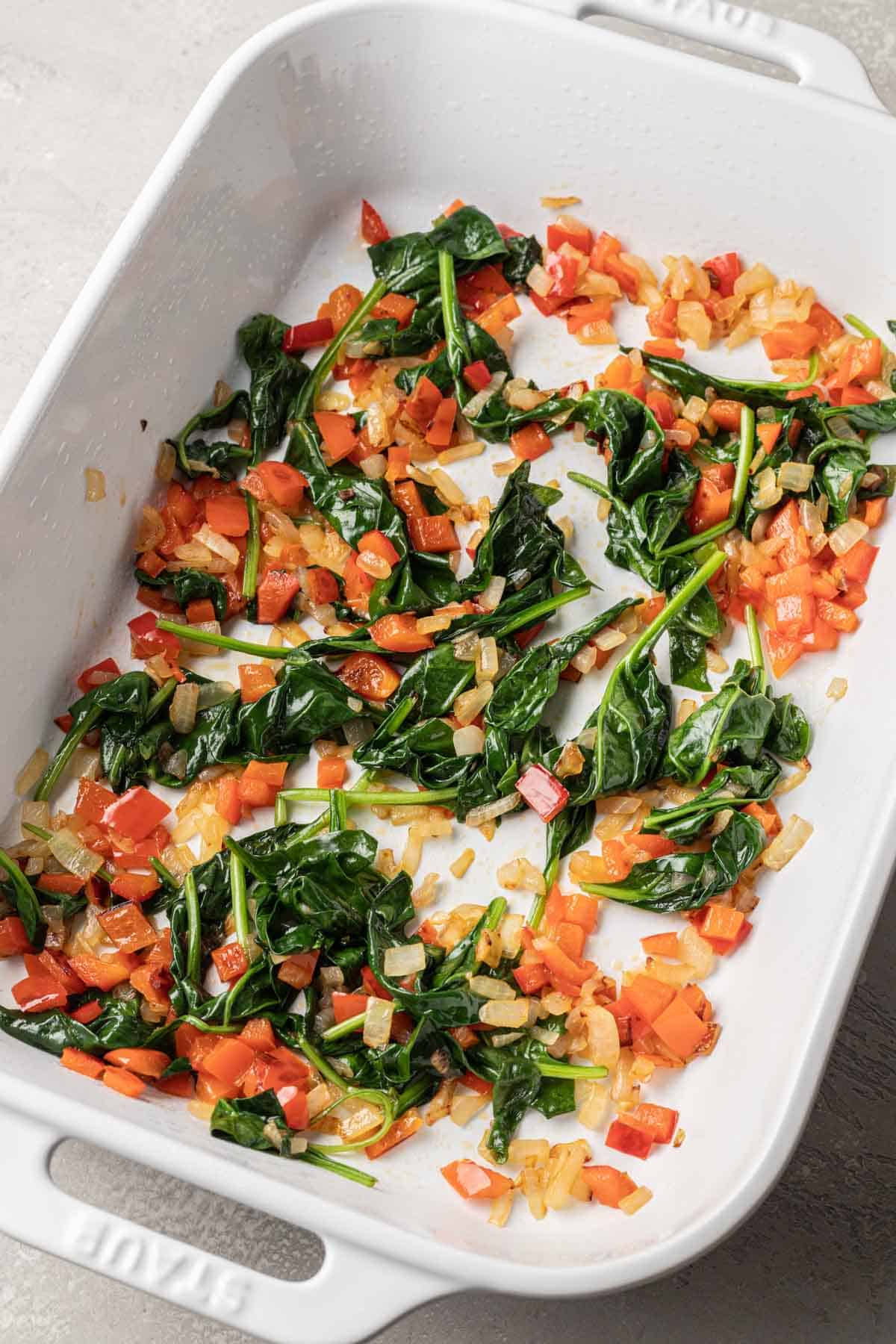 sautéd veggies in the bottom of a white casserole dish.
