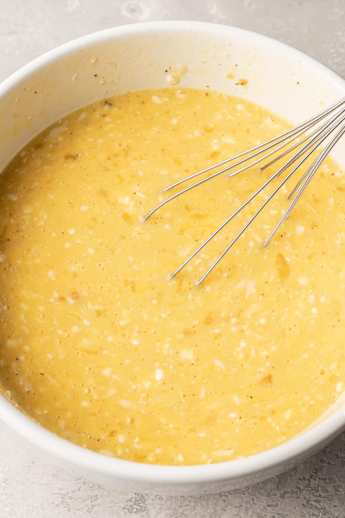 eggs and cottage cheese mixed together in a white bowl with a metal whisk.