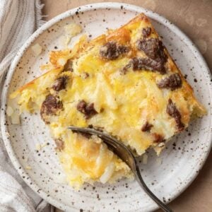 slice of dairy free breakfast casserole on a white plate with a fork taking a piece out of it.