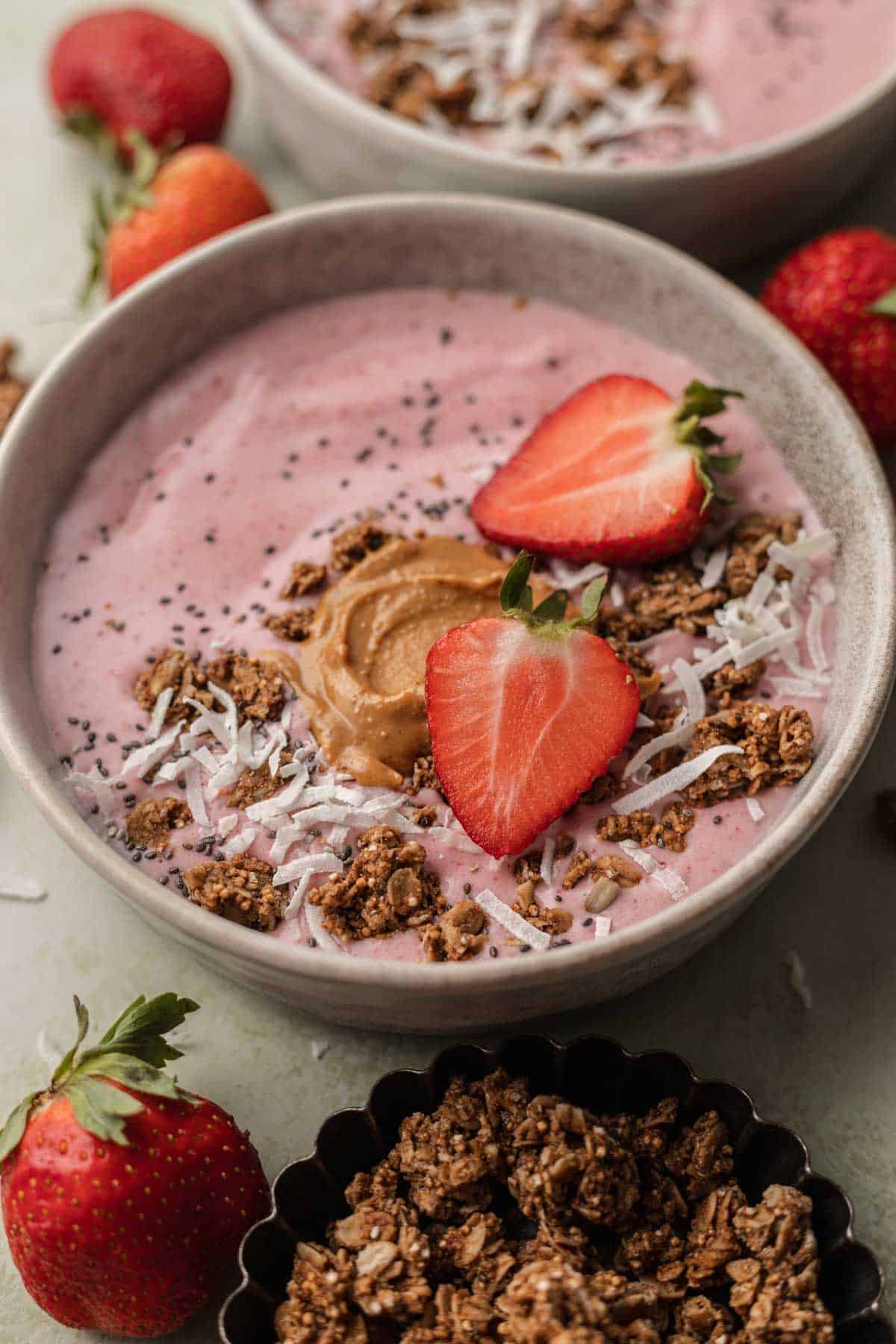 Strawberry smoothie bowl in ceramic bowl topped with fresh strawberries, coconut flakes, peanut butter and granola.