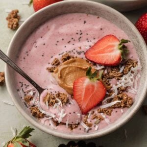 Freshly made strawberry smoothie bowl topped with fresh strawberries, coconut flakes and granola.