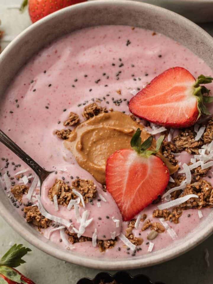 Freshly made strawberry smoothie bowl topped with fresh strawberries, coconut flakes and granola.