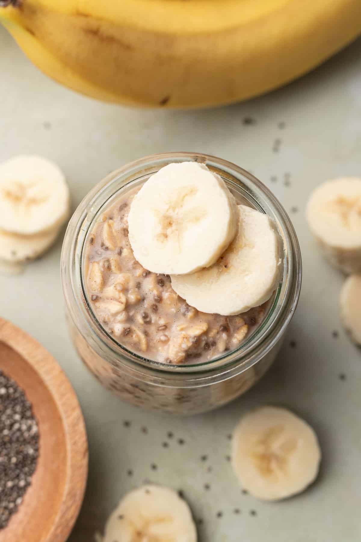 overhead view of banana chia overnight oats in a glass jar with chia seeds and sliced bananas around it.