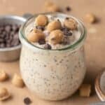 cookie dough overnight oats in a glass jar topped with cookie dough bites and mini chocolate chips.
