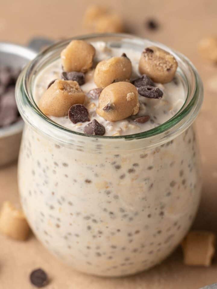 cookie dough overnight oats in a glass jar topped with cookie dough bites and mini chocolate chips.