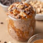 snickers overnight oats in a class jar topped with peanuts, chocolate chips, and a drizzle of caramel.