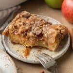 slice of apple french toast casserole covered with syrup on a plate with bites taken out of it.