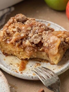slice of apple french toast casserole covered with syrup on a plate with bites taken out of it.