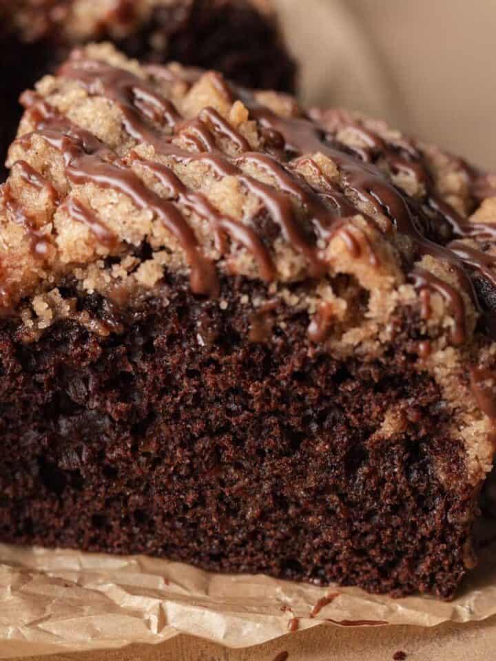 slice of chocolate coffee cake with streusel on top drizzled with chocolate icing.
