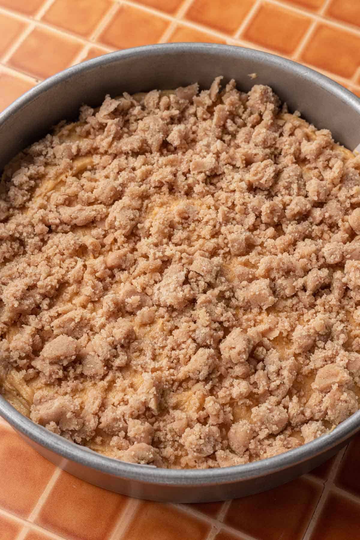 pumpkin coffee cake batter and streusel in a round baking pan before being baked.