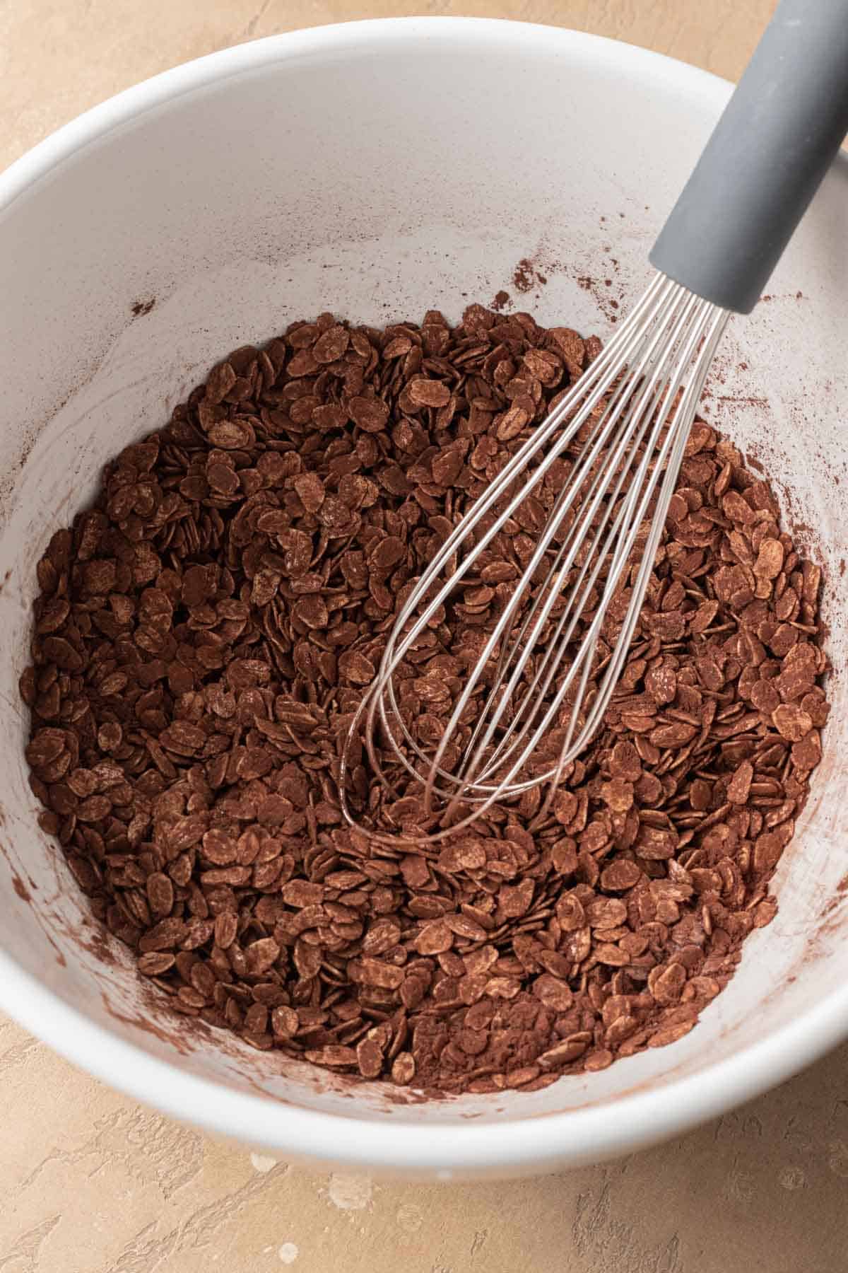 oats mixed with cocoa powder in a white bowl with a metal whisk.