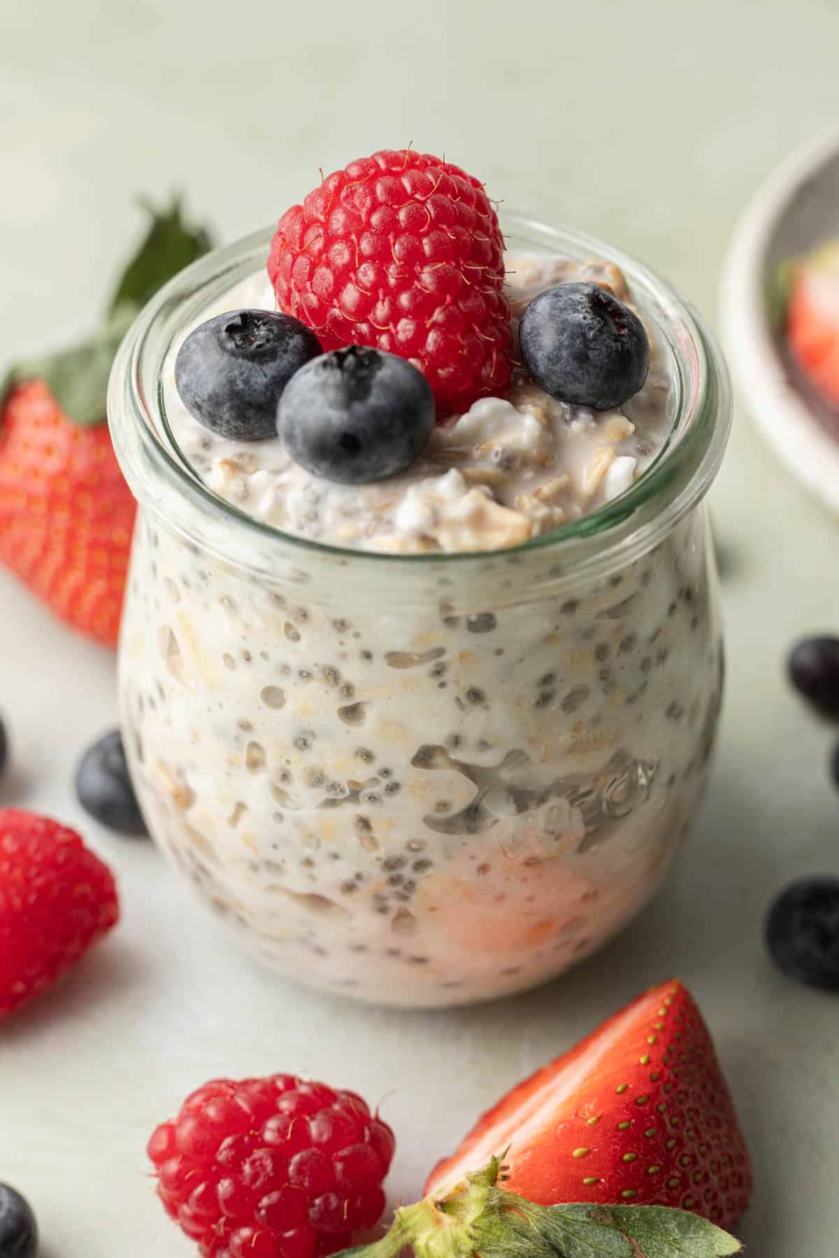glass car of cottage cheese overnight oats surrounded by fresh berries.