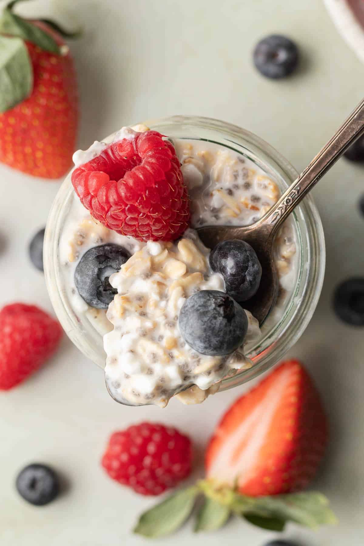 spoonful of cottage cheese overnight oats being scooped out of jar with fresh berries