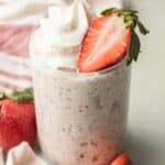 strawberry shortcake overnight oats in a clear jar topped with whipped cream and fresh strawberries.