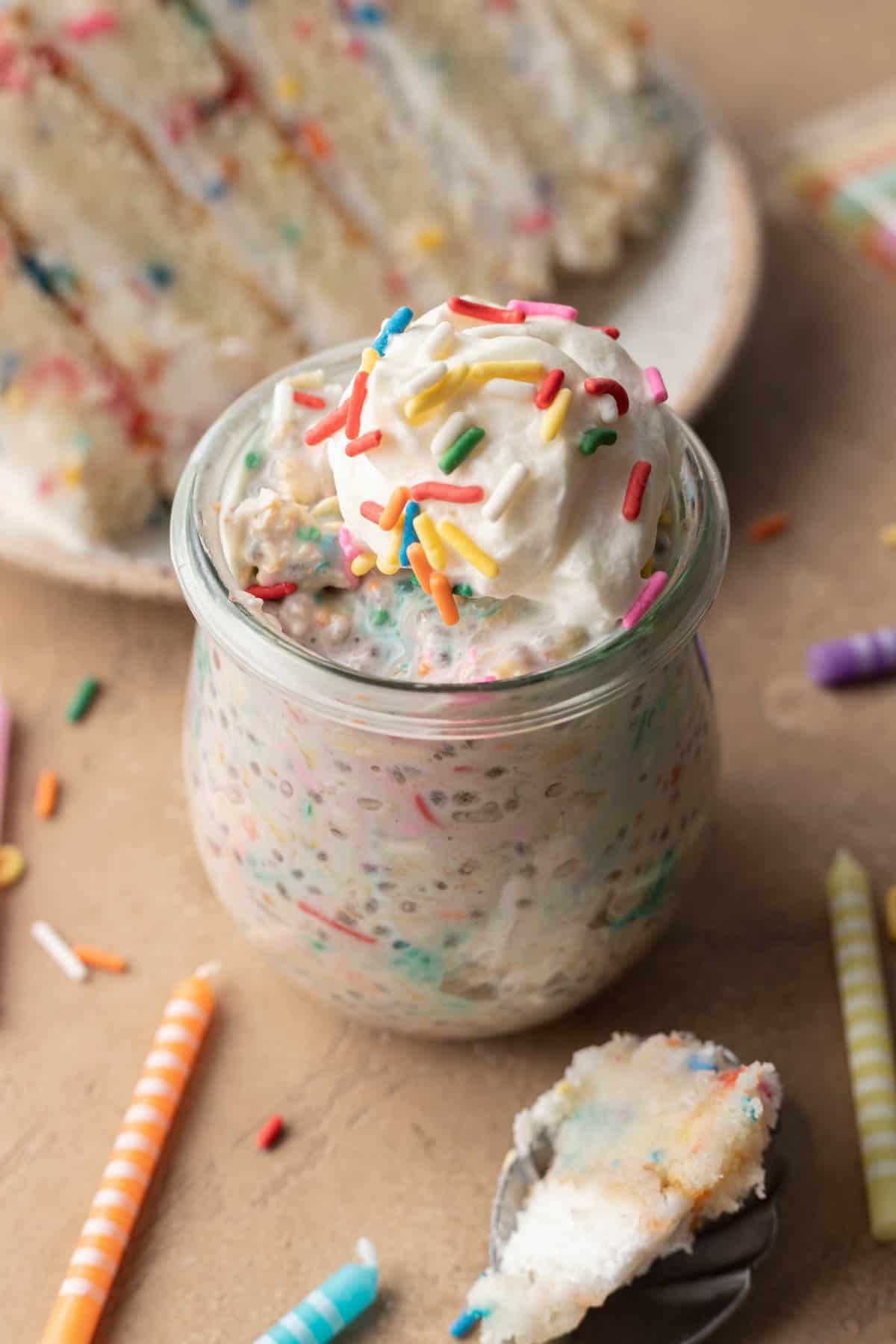 birthday cake overnight oats in a glass jar surrounded by birthday candles and birthday cake.