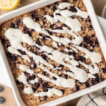 overhead view of blueberry lemon baked oats in a white dish, with lemon yogurt icing drizzled on top.
