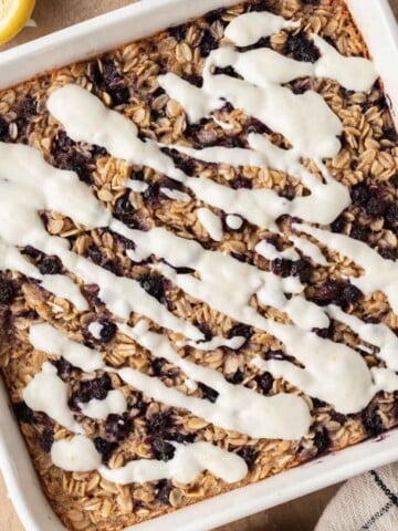 overhead view of blueberry lemon baked oats in a white dish, with lemon yogurt icing drizzled on top.