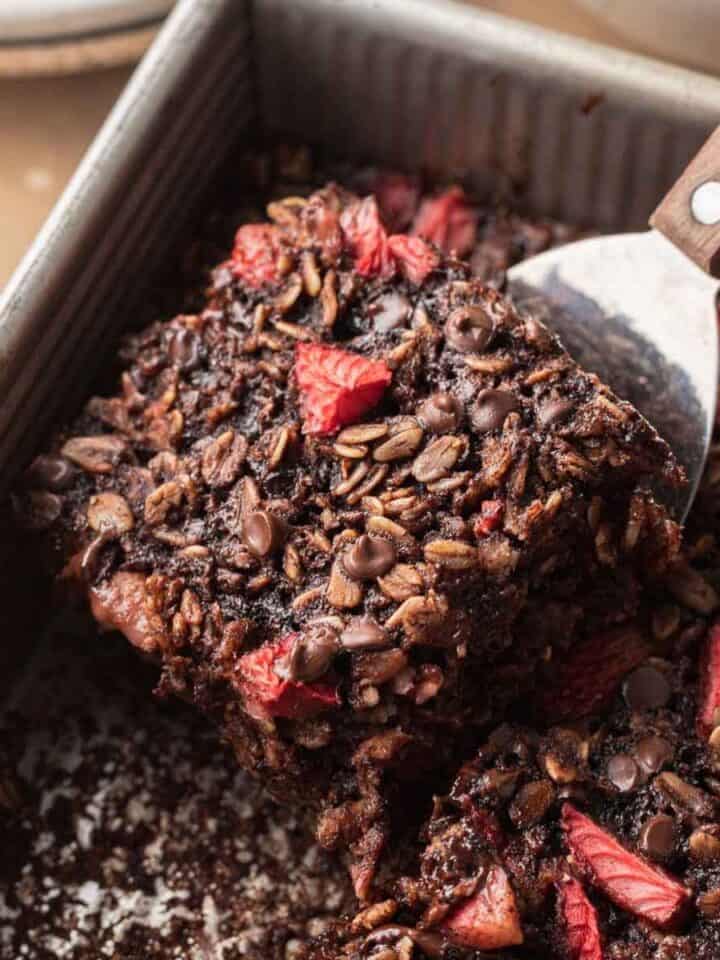 a slice of chocolate strawberry baked oatmeal being scooped out of baking dish.