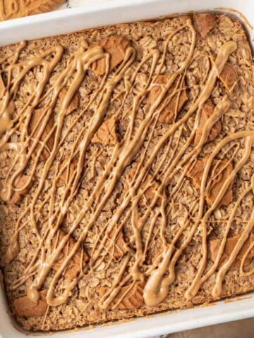 A square white pan featuring biscoff baked oats, topped with crushed cookies and drizzled biscoff spread.