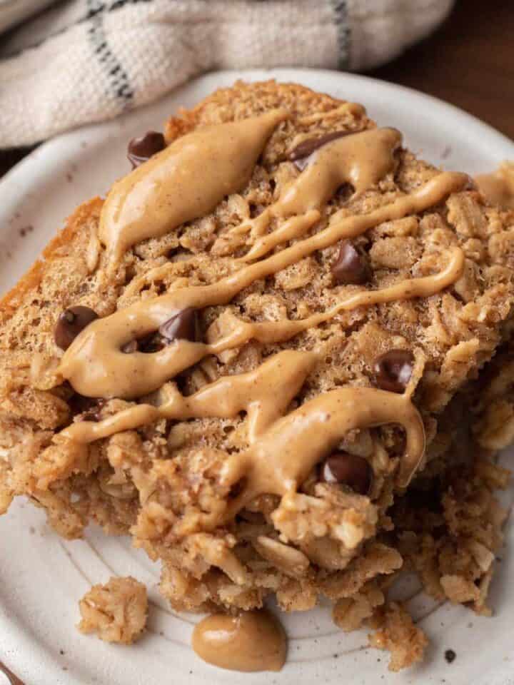 A slice of peanut butter baked oats crowned with chocolate chips rests invitingly on a white plate.