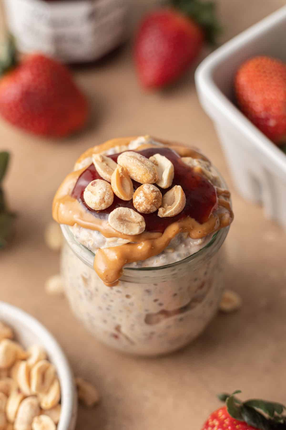 A jar of delightful pb&j overnight oats is accompanied by a medley of strawberries and a dish filled with crunchy peanuts, creating a wholesome breakfast symphony.
