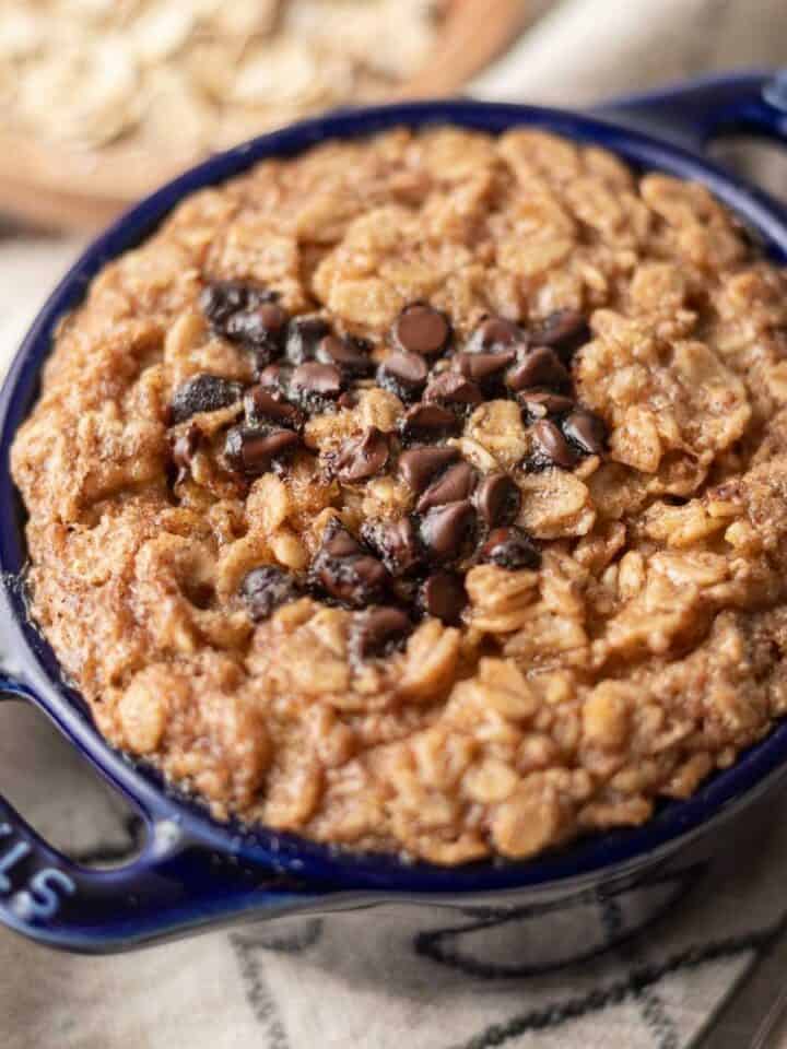 Single-serve baked oatmeal with chocolate chips sits invitingly in a blue dish on a patterned cloth.
