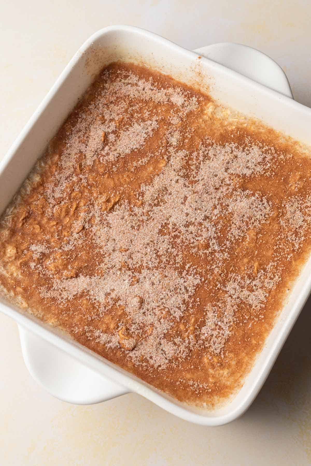 A white baking dish filled with oatmeal, topped with a layer of cinnamon sugar.
