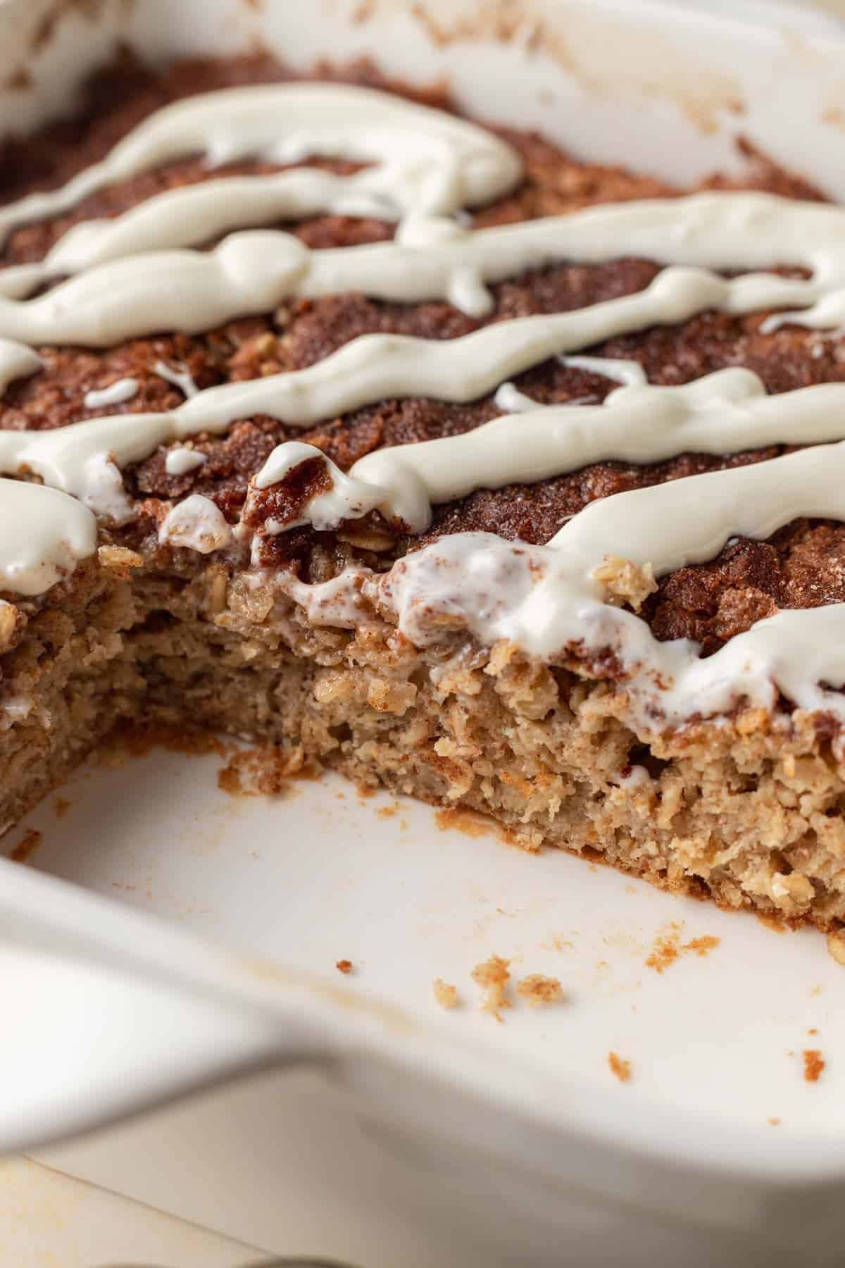 Baked oatmeal with white icing drizzle in a dish, with a portion cut out from one corner.