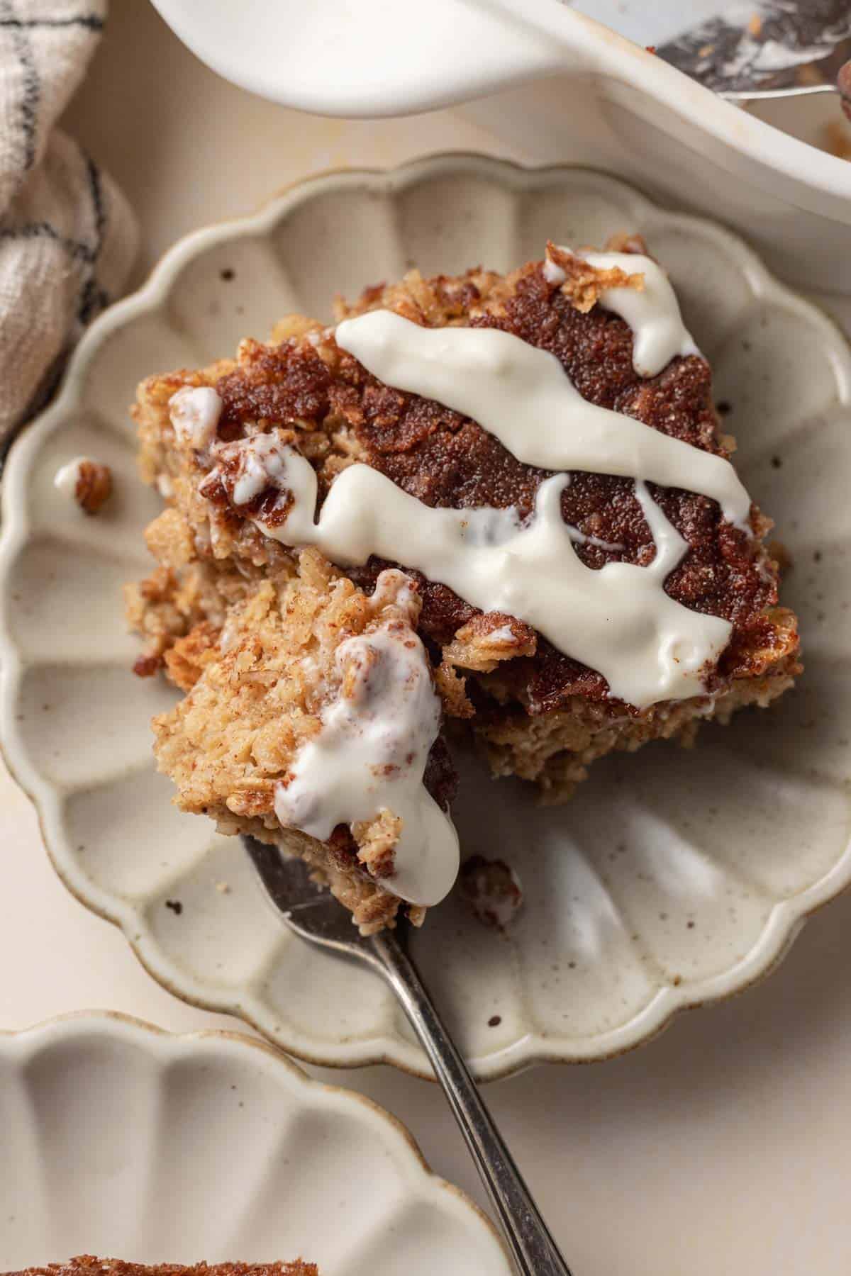 A slice of cinnamon coffee cake with white icing drizzled on top, served on a plate with a fork.