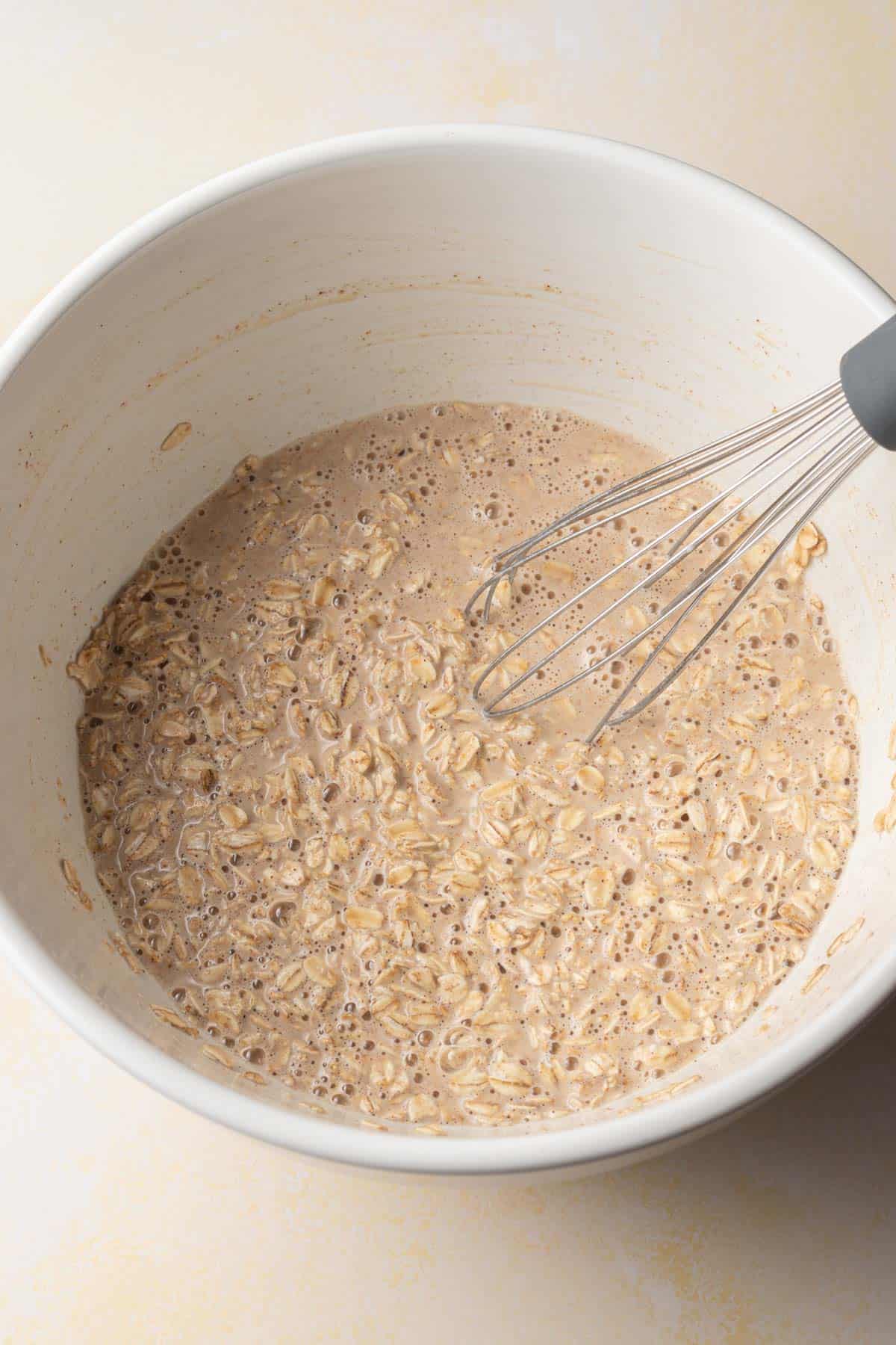 A whisk in a bowl of mixed oats and liquid, creating a bubbly oatmeal batter.