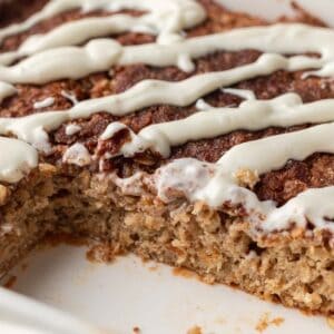 Close-up of baked oatmeal topped with white icing, with a slice missing from the corner.