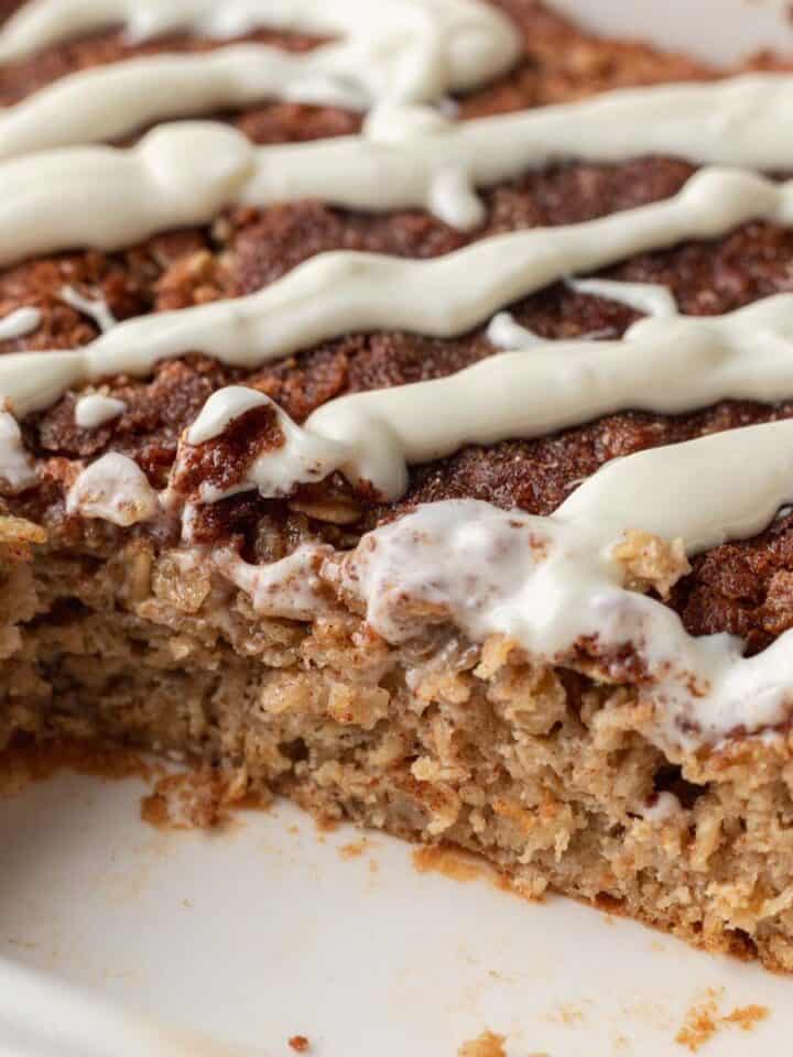 Close-up of baked oatmeal topped with white icing, with a slice missing from the corner.