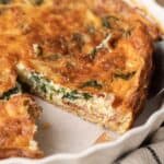 A close-up of a sliced quiche with spinach and cheese in a white pie dish.
