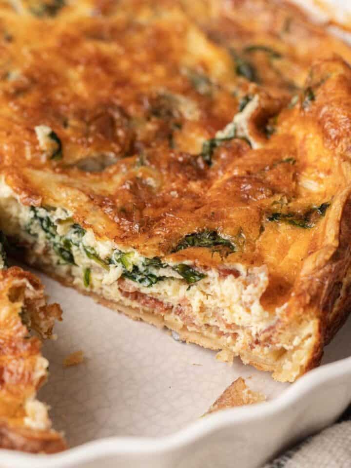 A close-up of a sliced quiche with spinach and cheese in a white pie dish.