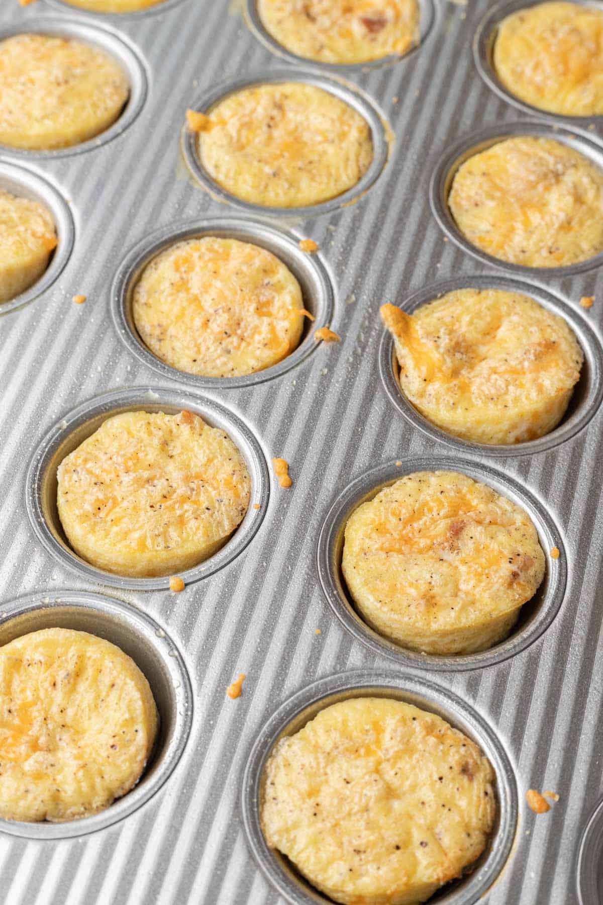 Mini egg and cheese muffins in a metal muffin tin, lightly browned and seasoned with pepper.