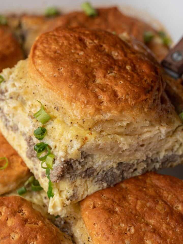 A slice of casserole with layers of biscuit, sausage, and egg, topped with chopped green onions.
