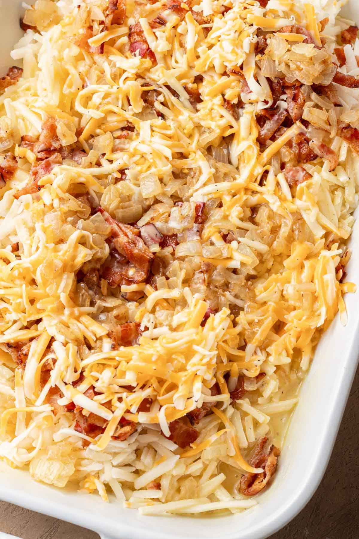 Shredded cheese, bacon, and cooked onions layered in a white baking dish.