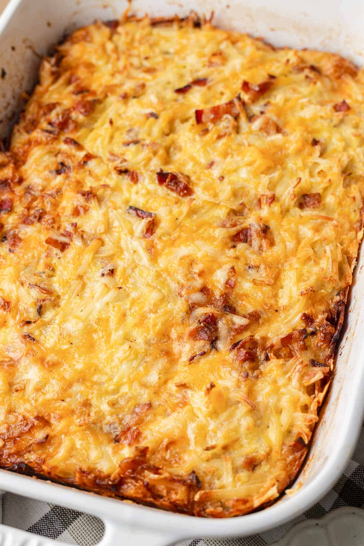 Golden cheesy hash brown casserole baked in a white rectangular dish with a slightly crispy top.