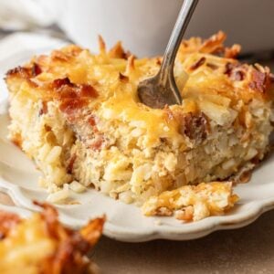 A fork cutting into a cheesy, golden hash brown casserole served on a white plate.
