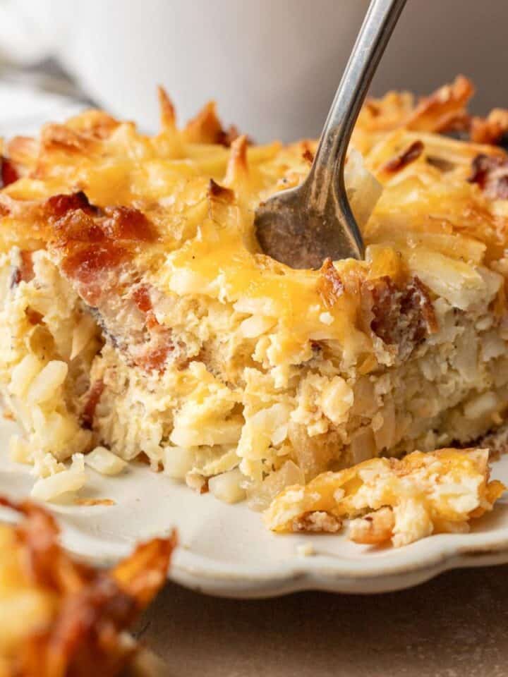 A fork cutting into a cheesy, golden hash brown casserole served on a white plate.